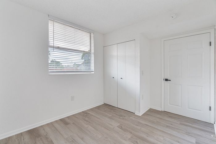 Bright bedroom with modern laminate flooring, large window with blinds, and a sleek built-in closet.
