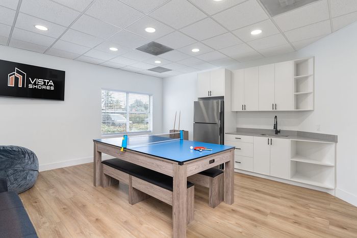 Modern recreational room with a stylish table tennis setup, sleek kitchenette, and cozy seating under bright ceiling lights, perfect for entertainment at Vista Shores.