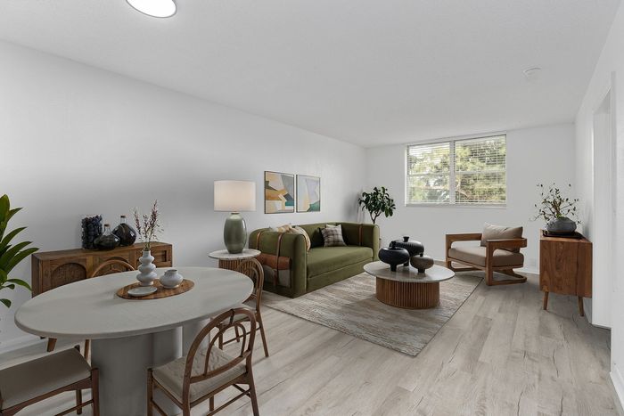 Bright and inviting living-dining area with stylish wood flooring, chic furniture, and abundant natural light streaming through large windows.