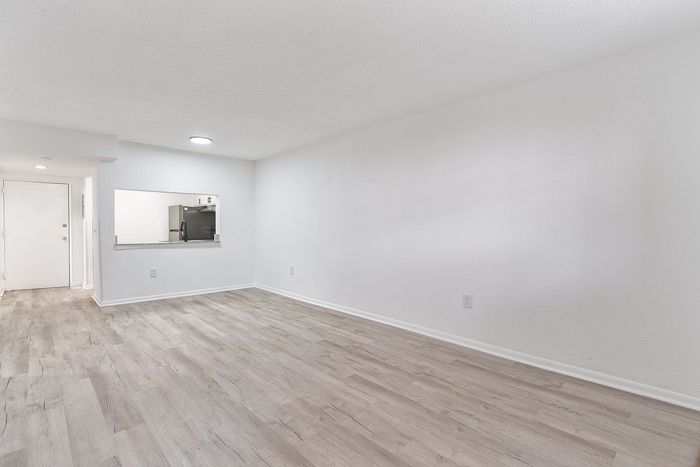Spacious open-concept living room with elegant hardwood flooring and a peek-through window to the modern kitchen.