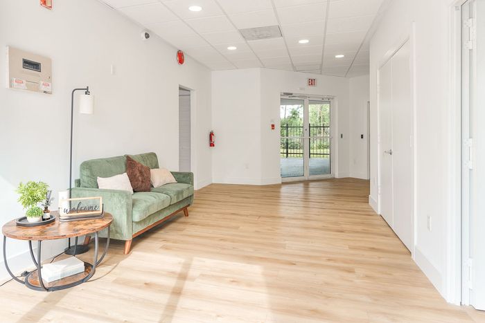 Bright and inviting living area with modern decor, featuring a cozy green sofa and a stylish wooden floor, leading to large windows with garden views.