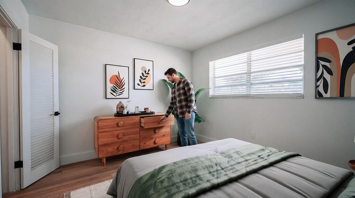 Bright, inviting bedroom with modern decor featuring a stylish wooden dresser, cozy bed, and artistic wall prints.