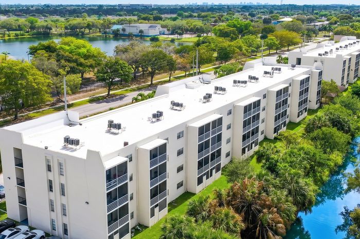 Expansive aerial view of Canal Views Residences, showcasing sleek white apartment buildings surrounded by lush greenery and a serene canal, ideal for luxury living.