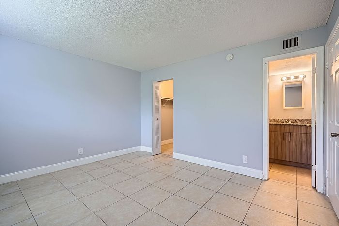 Bright and airy room with sleek tiled flooring, direct access to a walk-in closet, and an adjoining bathroom with stylish lighting.