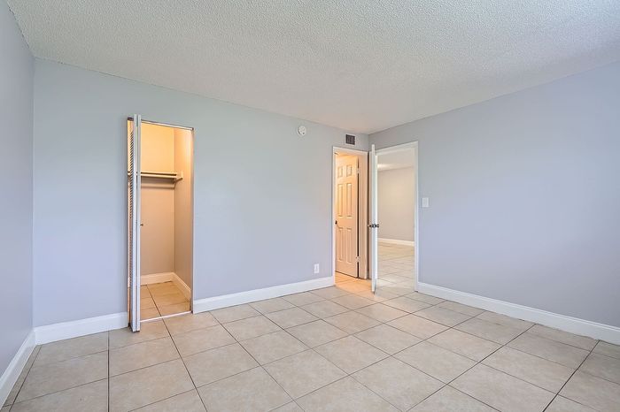 Bright bedroom with tiled floors, a spacious closet, and soft gray walls, offering a modern and inviting ambiance.
