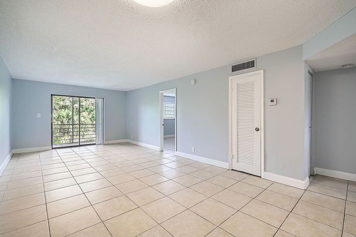 Bright unfurnished living room with large window overlooking greenery, featuring soft blue walls and elegant tile flooring.