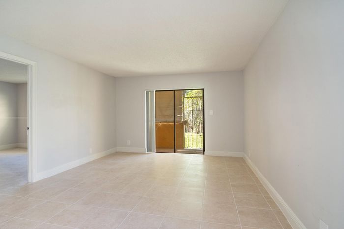 Bright and airy living room with large sliding doors leading to a serene outdoor view, featuring polished tile flooring and soft neutral walls.