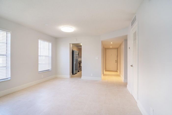 Bright and inviting living space with modern kitchen, sleek tile flooring, and abundant natural light through large windows.