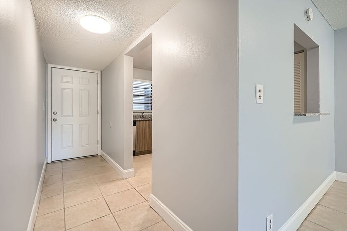 Inviting apartment entryway featuring stylish tile flooring and modern light fixtures leading into a well-lit kitchen area with a view of elegant cabinetry.