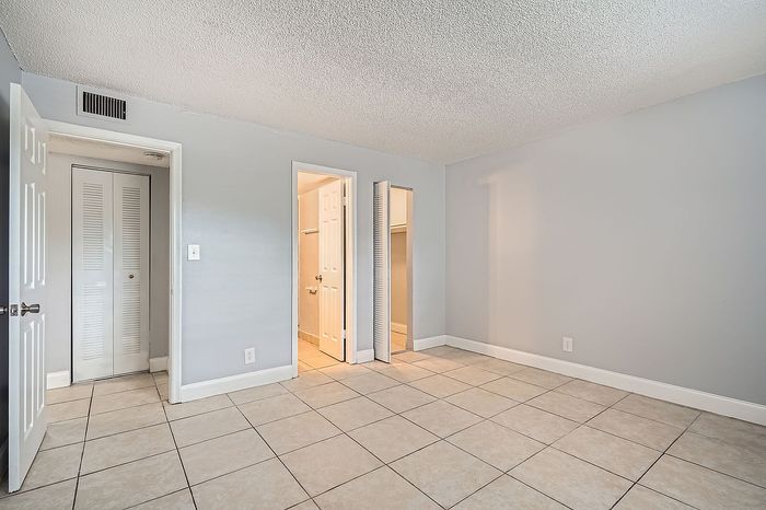 Bright, spacious room with elegant tiled flooring, featuring a closet and access to a convenient en-suite bathroom.