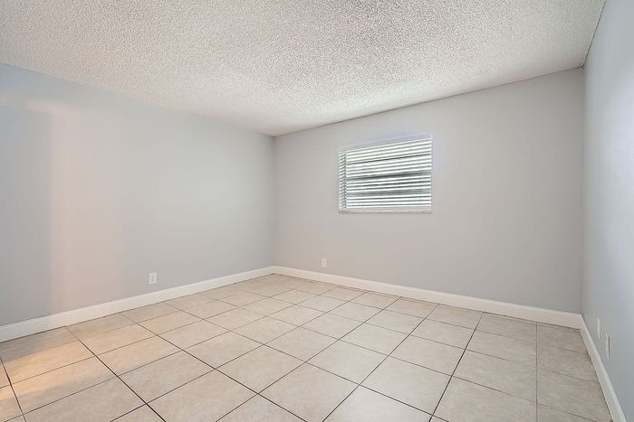 Bright and airy room with elegant tiled flooring and a large window, offering a versatile space for stylish living.