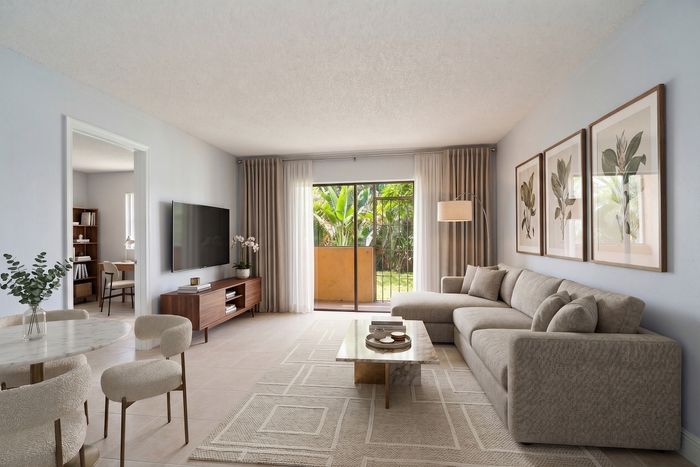 Elegant living room with a cozy beige sectional, stylish decor, and large glass doors opening to a lush garden view.