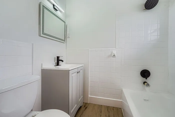 Bright and modern bathroom featuring sleek white tile, a stylish vanity with black fixtures, and a luxurious rainfall showerhead.