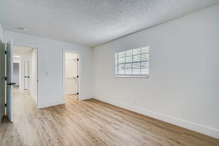Bright, spacious room with elegant wood flooring, neutral walls, and ample natural light from the large window, perfect for a cozy bedroom environment.