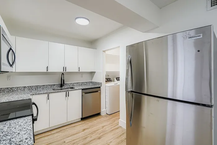 Modern kitchen with sleek stainless steel appliances, spacious granite countertops, and ample white cabinetry, adjacent to a cozy laundry nook.