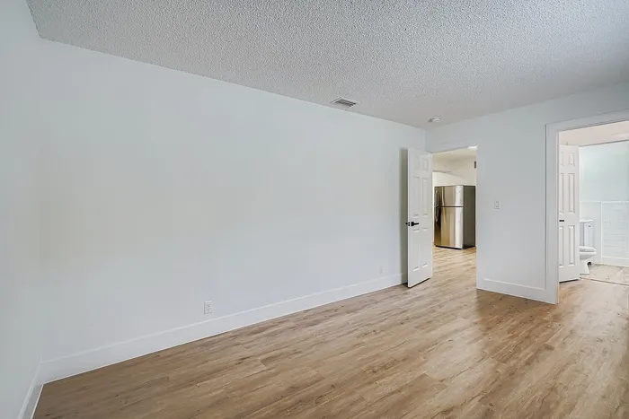 Spacious room with elegant wood flooring and modern open doorways, leading to a sleek kitchen and bright bathroom.