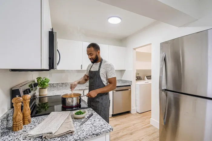 Modern kitchen with sleek granite countertops and stainless steel appliances, featuring a cheerful chef cooking a delicious meal.