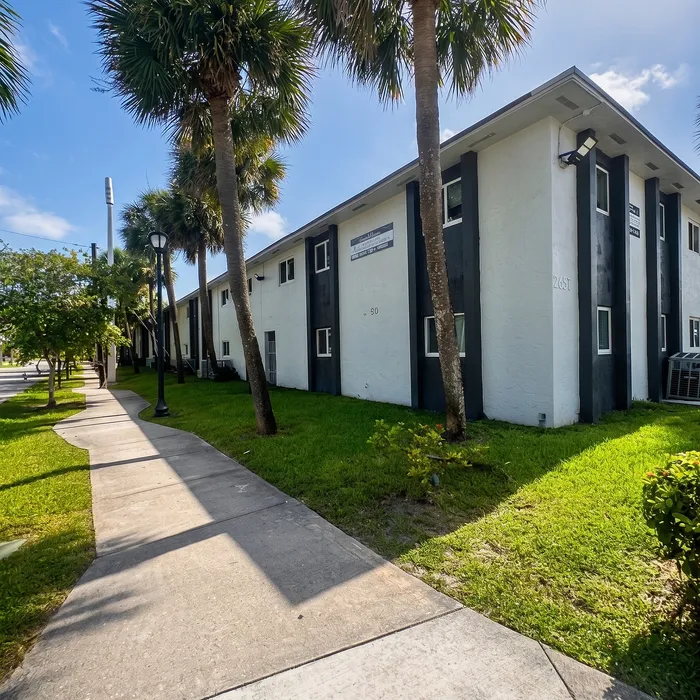 Charming apartment building with modern exterior nestled amidst lush greenery and palm trees, offering a serene and inviting atmosphere.