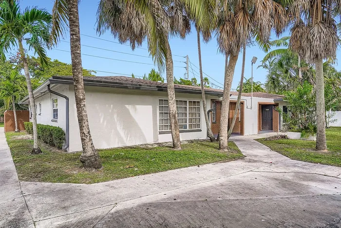 Charming single-story home with lush palm trees, spacious windows, and inviting pathways in a serene neighborhood.
