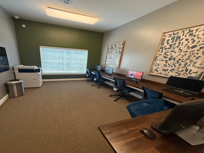 Contemporary workspace with multiple computer stations, abstract artwork, and a sleek printer, offering a productive environment.
