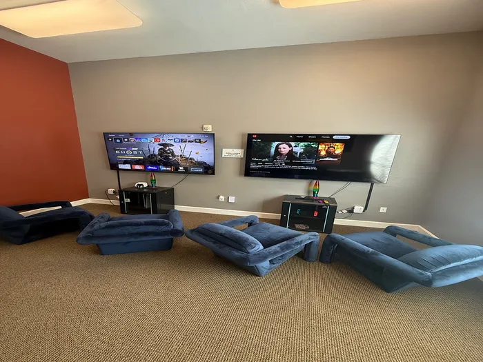 Inviting entertainment room with plush blue chairs, dual wall-mounted TVs, and relaxing ambiance.