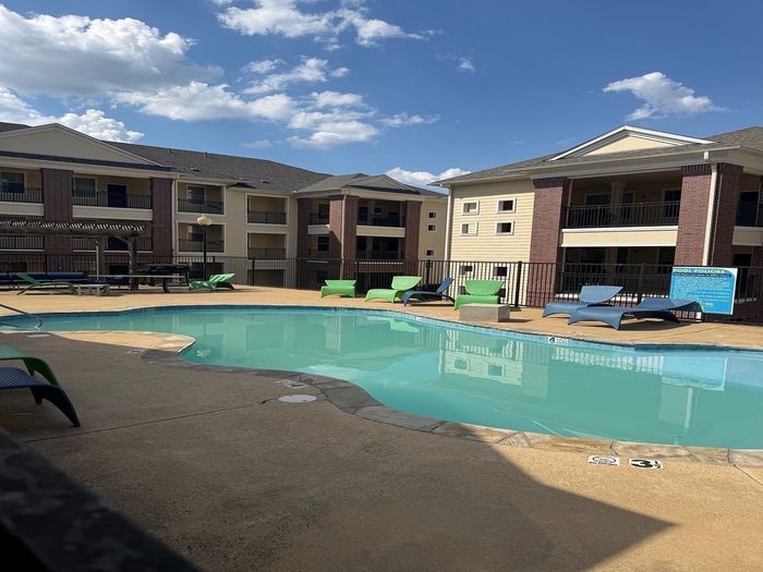 Charming residential complex with a sparkling outdoor pool, surrounded by modern architecture and inviting lounge chairs under a sunny sky.