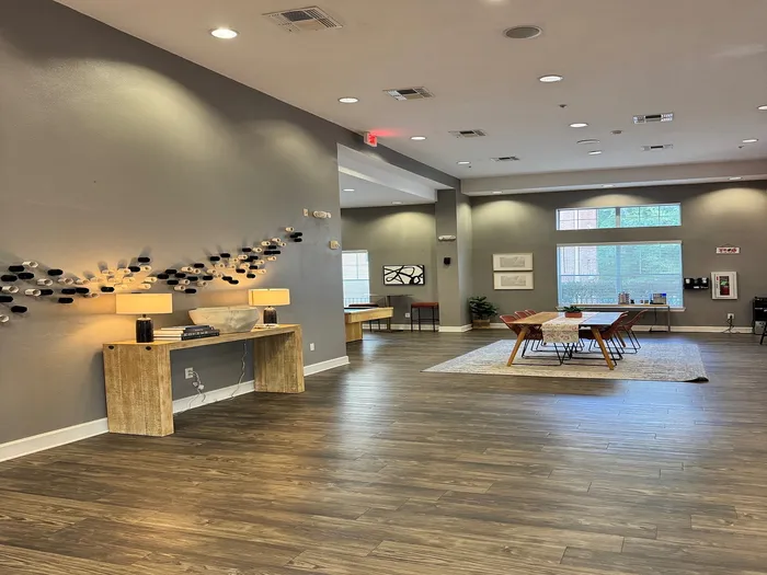 Chic and modern communal area with elegant wooden floors, ambient lighting, and stylish wall decor. Features a spacious dining table, cozy seating, and large windows for natural light.