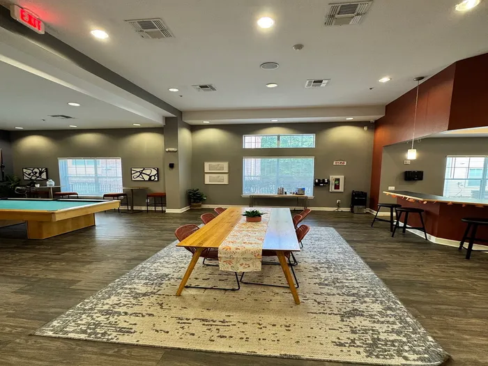 Modern open-concept recreation room with elegant lighting showcasing a stylish dining area, chic bar stools, and a pool table, all set on rich wooden floors.