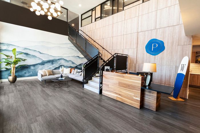 Modern lobby with elegant wood accents, stylish staircase, and a chic seating area beneath artistic wall mural.
