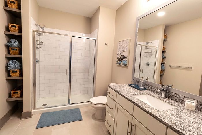 Elegant bathroom featuring a spacious glass shower, sleek granite countertop, and modern storage shelves with woven baskets.