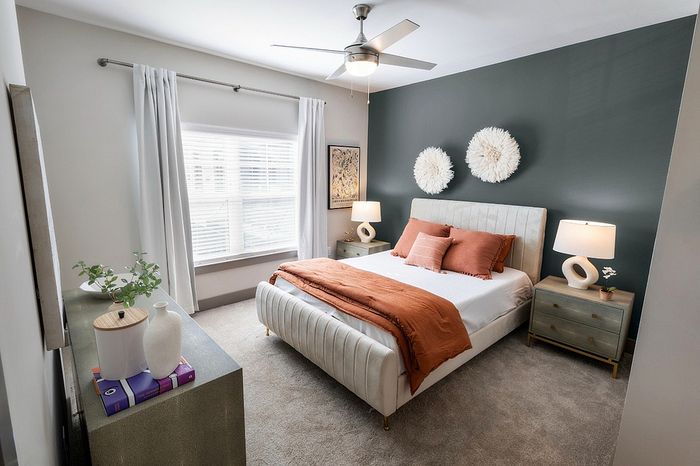 Elegant bedroom with a modern design featuring a plush bed, decorative cushions, stylish gray accent wall, and ample natural light from a large window.