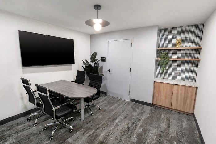 Modern conference room with sleek furnishings, featuring a large wall-mounted TV, stylish chairs, and a decorative shelving unit.