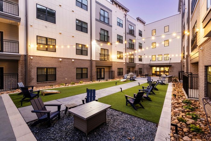 Charming courtyard at dusk with string lights, cozy seating, and lush greenery in a modern apartment complex.
