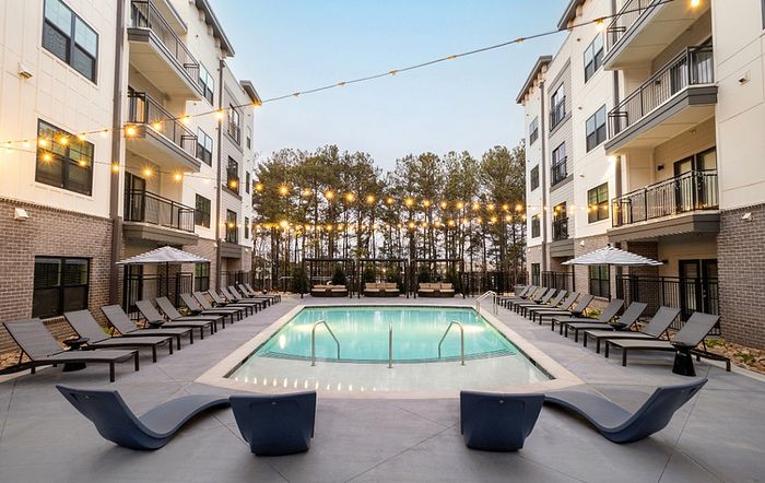 Luxurious apartment complex featuring a sparkling outdoor pool surrounded by elegant lounge chairs and charming string lights, perfect for relaxing evenings.