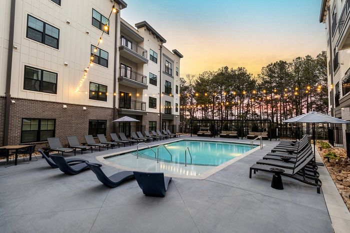 Contemporary apartment complex with a serene outdoor pool area, stylish lounge chairs, and ambient string lights at sunset.