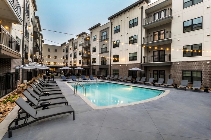 Luxurious apartment complex courtyard featuring a sparkling swimming pool, surrounded by stylish loungers and charming string lights for evening ambiance.