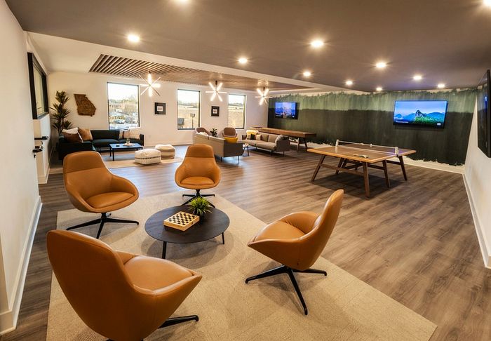 Elegant communal living area with modern leather seating, natural lighting, and entertainment options including a ping pong table and multiple TVs.