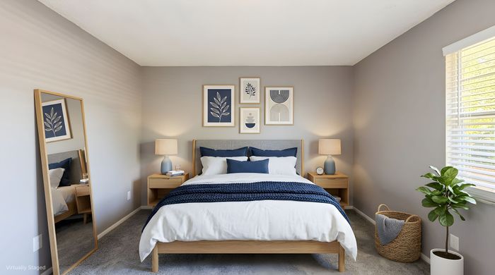 Elegant bedroom with modern decor, featuring a comfortable bed with navy accents, stylish artwork, a large mirror, and abundant natural light.