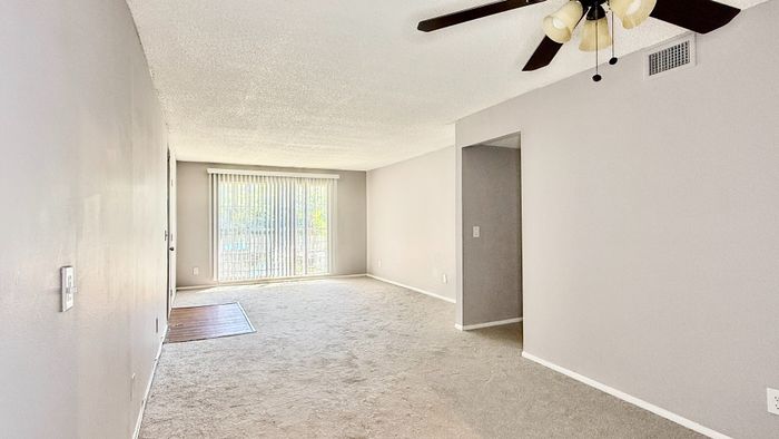 Bright and spacious living room with large window, elegant ceiling fan, and neutral tones, offering a cozy and inviting atmosphere.