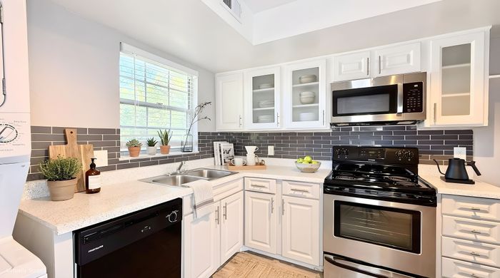 Beautifully designed kitchen with modern stainless steel appliances, chic gray subway tile backsplash, and elegant white cabinetry. Sunlit space enhanced with houseplants and stylish decor, perfect for culinary delights.
