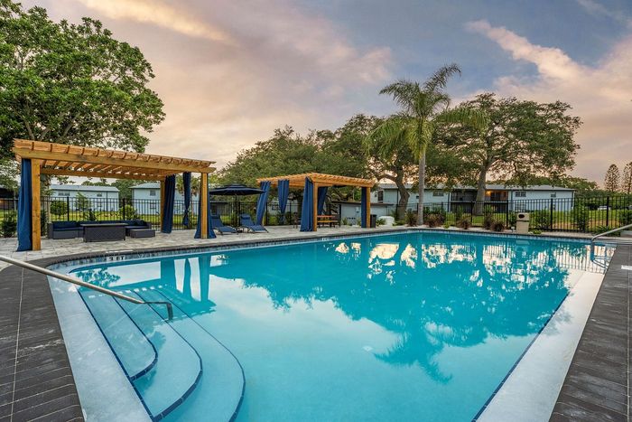 Inviting outdoor pool area featuring shaded pergolas, lush greenery, and comfortable lounge seating against a serene sky backdrop.