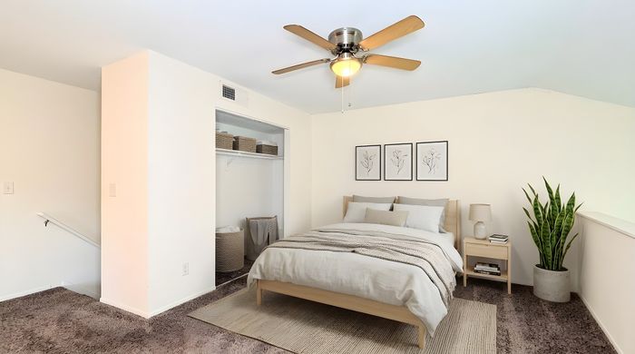 Chic bedroom with cozy beige decor, modern ceiling fan, open closet, and stylish greenery for a serene ambiance.