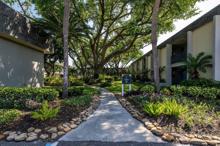 Charming apartment courtyard with lush greenery, mature trees, and inviting stone-lined pathways leading to modern buildings.