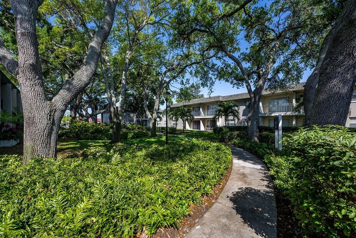Inviting apartment complex nestled among lush greenery and mature trees, offering a serene pathway and tranquil outdoor setting.
