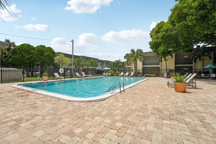 Inviting outdoor pool area with lush landscaping and comfortable lounge chairs, perfect for relaxation under the sunny sky.