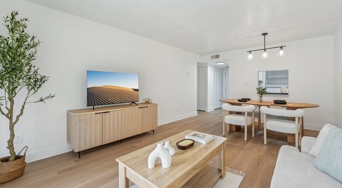 Bright and modern living-dining area with sleek wooden furniture, stylish decor, and a large TV, offering a warm, inviting atmosphere.