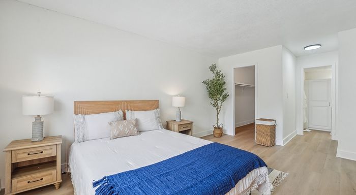 Bright and inviting bedroom with modern decor, featuring a cozy bed, stylish nightstands, and a lush potted plant complementing the serene white walls.