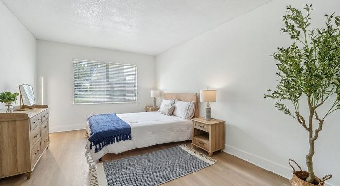 Bright and cozy bedroom with modern decor, featuring a comfortable bed, stylish wooden furniture, and a decorative plant for a refreshing ambiance.