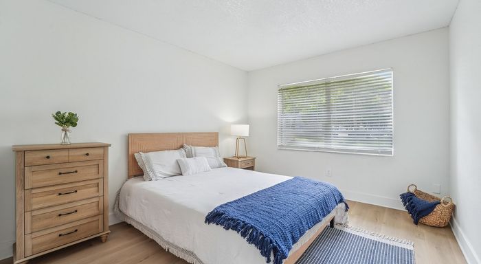 Bright and airy bedroom featuring elegant wood furniture, plush bedding, and a large window bringing in natural light.