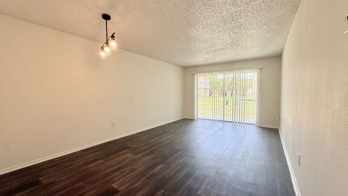 Bright and spacious living room with elegant wood flooring and large sliding glass doors opening to a lush garden view.